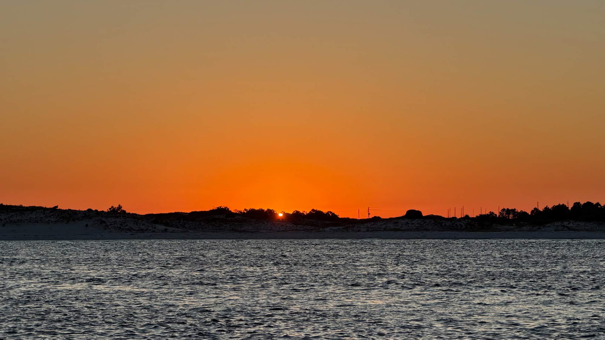 Sunset over the Destin Gulf with an orange sky and distant silhouetted shoreline.