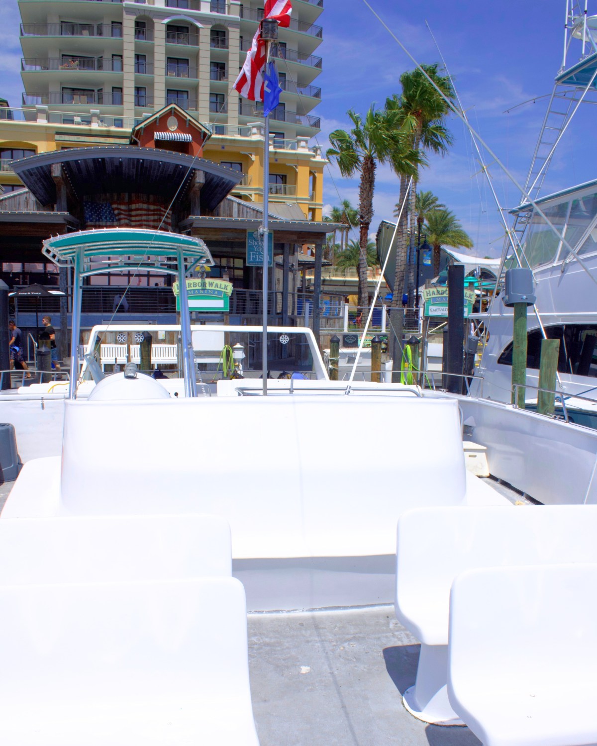 Empty boat with white seats docked near buildings and palm trees.