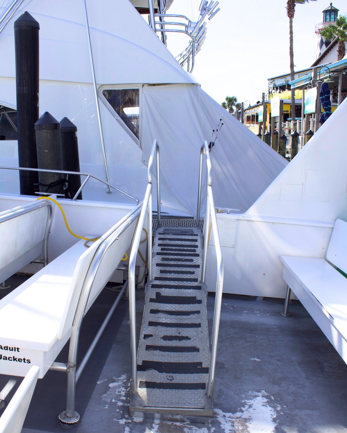 Stairs with metal railing on a boat near benches and dockside view.