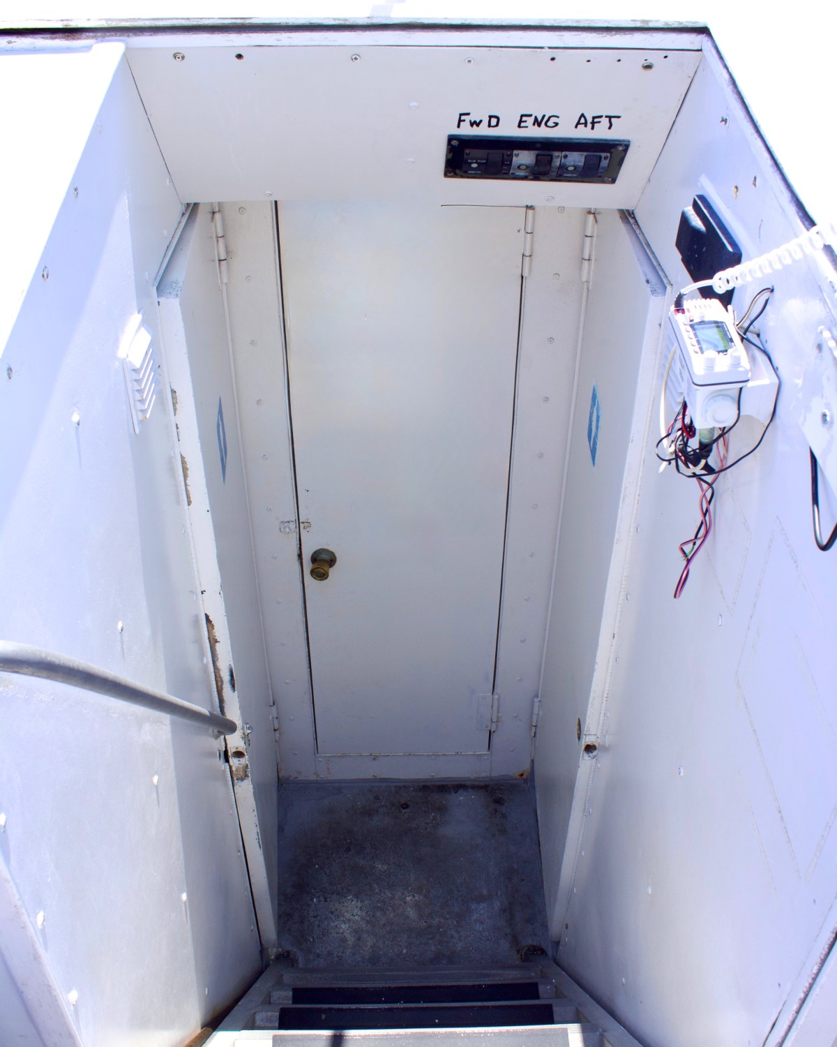 Narrow stairwell with metal walls leading to a closed door.