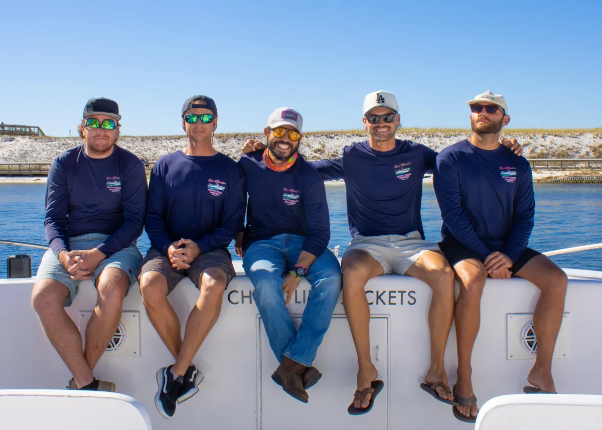 Five men in blue shirts sitting on a boat in sunny weather.