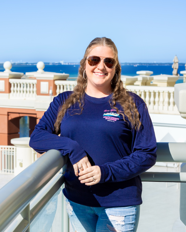 Person in sunglasses and blue shirt on rooftop with ocean view.